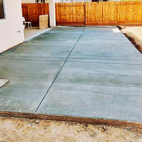 A brand new concrete patio in a backyard with wood fence surrounding the space